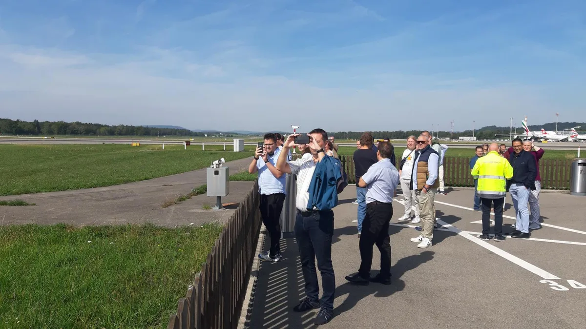 Bei Pistenkreuz durften die Fahrgäste für ein paar Minuten aussteigen. , Mit dem Car fuhren die Dübendorfer zum Flughafen. , So geht Lokalpatriotismus: Cornelia Schwarz und ihr Mann Blacky lotsen die Reisegruppe mit Dübi-Fähnchen durch das Areal., Die Landung eines A380 aus unmittelbarer Nähe war einer der Höhepunkte der Rundfahrt. , Die Geräuschkulisse direkt neben einem startenden Flieger war beeindruckend. , Cornelia Schwarz' Kurzansprache beim Apéro Nummer 1. , Einer der drei Rega-Jets im Hangar: Wegen Wartungsarbeiten durften die Besucher das Flugzeug nicht betreten. , Das ausgebaute Triebwerk eine Rettungshelis wird gewartet., Beim Besuch in der Rega-Einsatzzentrale konnten die Anwesenden verfolgen, wo die Rega gerade einen Einsatz fliegt. , Apéro Nummer 2 im Restaurant Alter Tobelhof. , Gruppenfoto in Gockhausen.