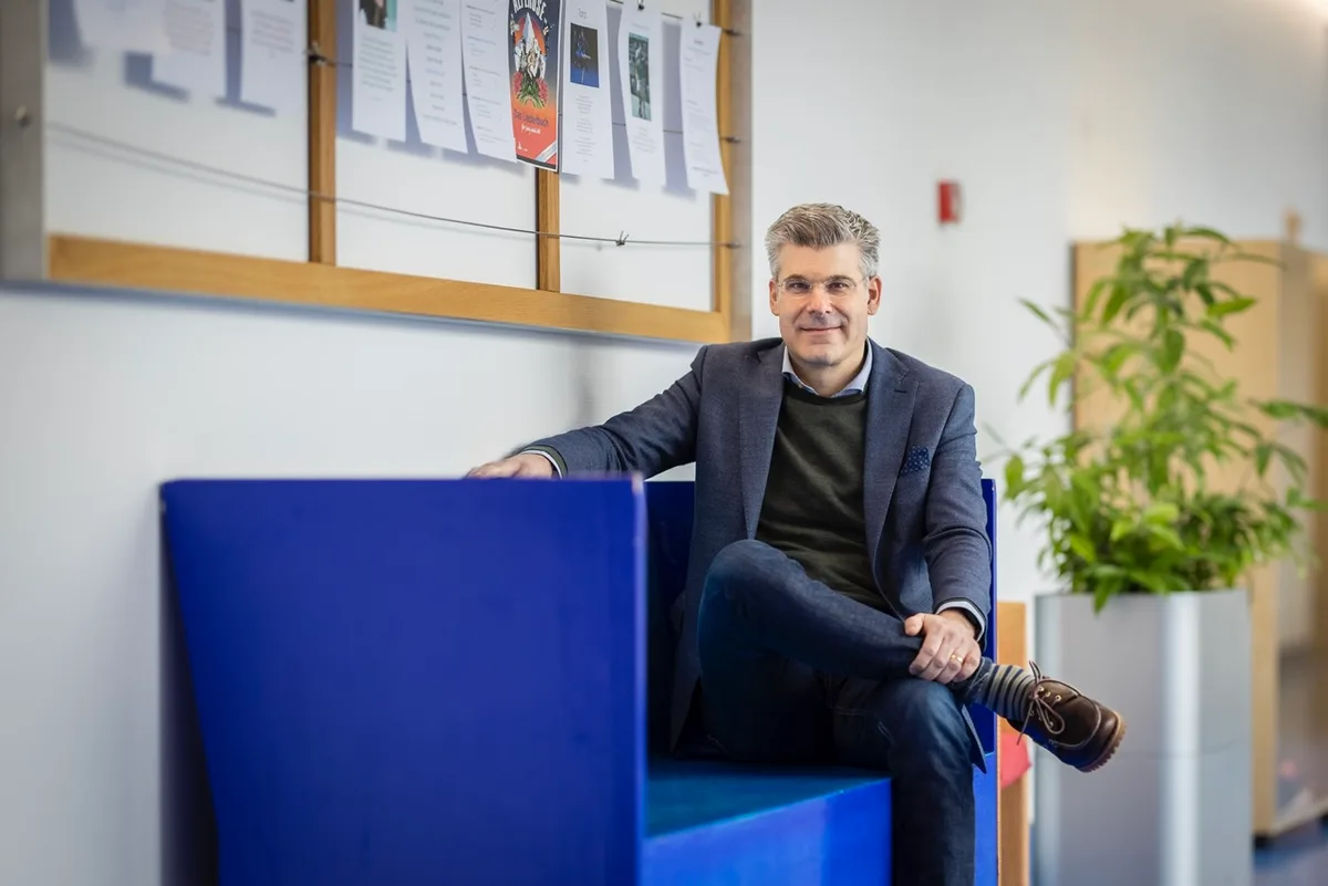 Dr. Markus Baumgartner sitzt auf einer blauen Sitzbank. 