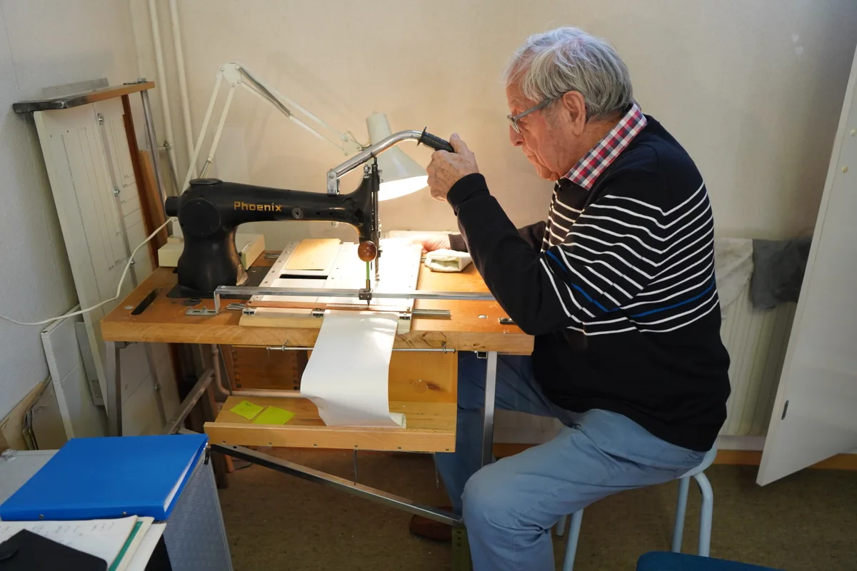 Mit einer Nähmaschine stanzt er die Löcher ins Notenband. Foto: gap Ein älterer Mann sitzt an einer antiken Phönix Nähmaschine und stanzt damit Löcher in ein Band