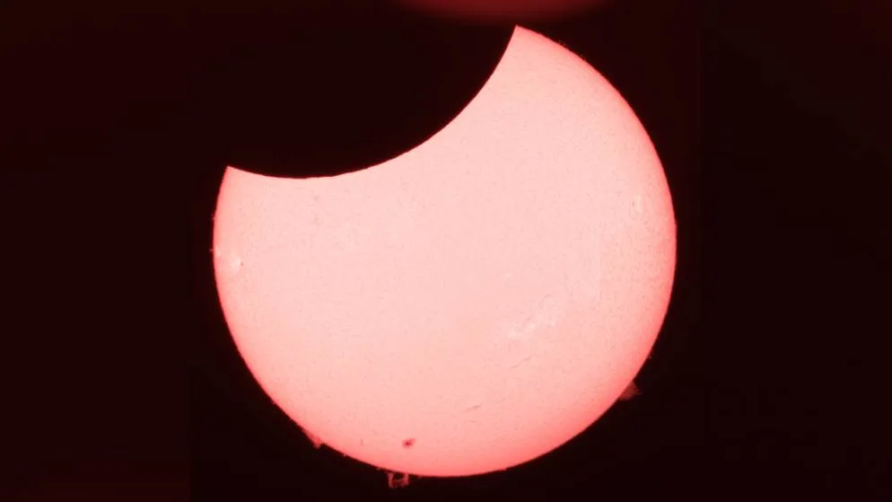 Die Sonnenscheibe zeigt sich hier deutlich vom Mond angeknabbert, am unteren Rand sind Gasauswürfe zu sehen. , Mit den richtigen Schutzfiltern vor den Objektiven eignet sich sogar ein Fernglas für das Mitverfolgen einer Sonnenfinsternis.