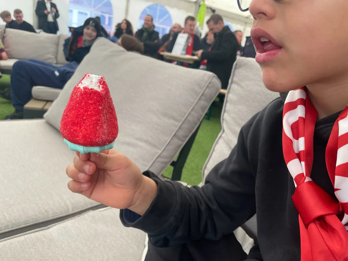 Kind mit offenem Mund hält eine angebissene Schaumerdbeere in der Hand. 