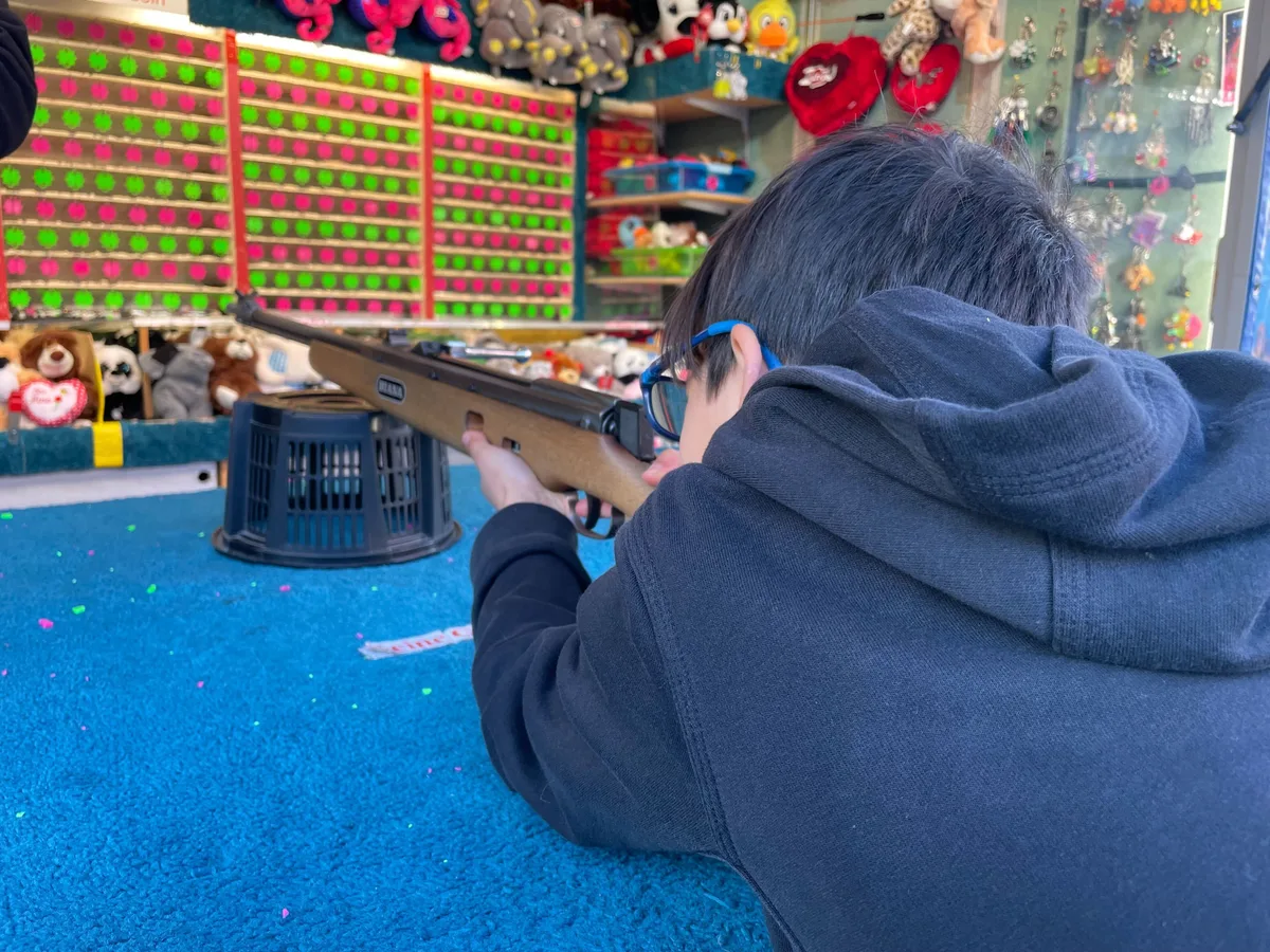 Junge (von hinten) hat ein Luftgewehr angelegt und schiesst auf Sterne. 