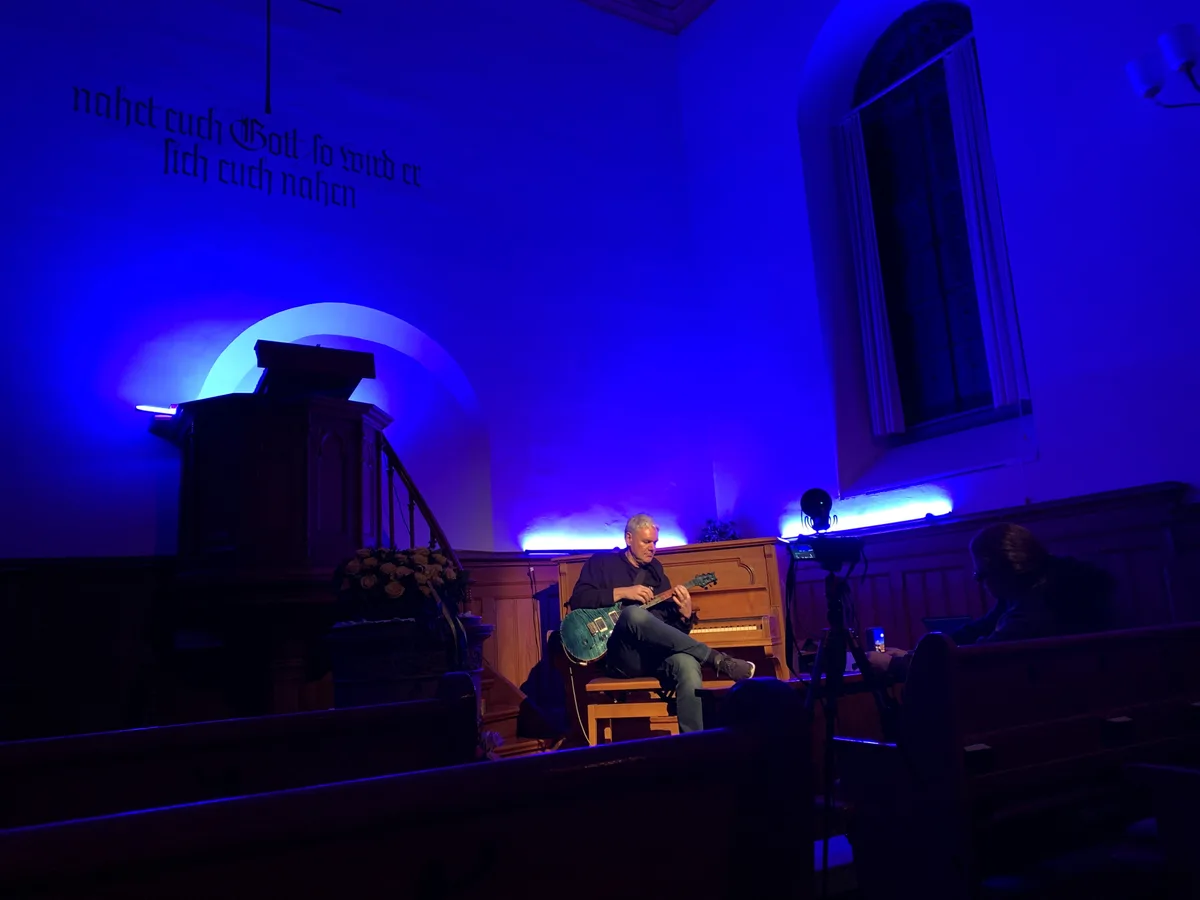 Warum nicht Pianospiel auf dem Gitarrenhals? Hanspeter Krüsi demonstriert seine Virtuosität. In der in Blau getauchten Kirche Seegräben sitzt Hanspeter Krüsi vor dem Piano und spielt Gitarre.