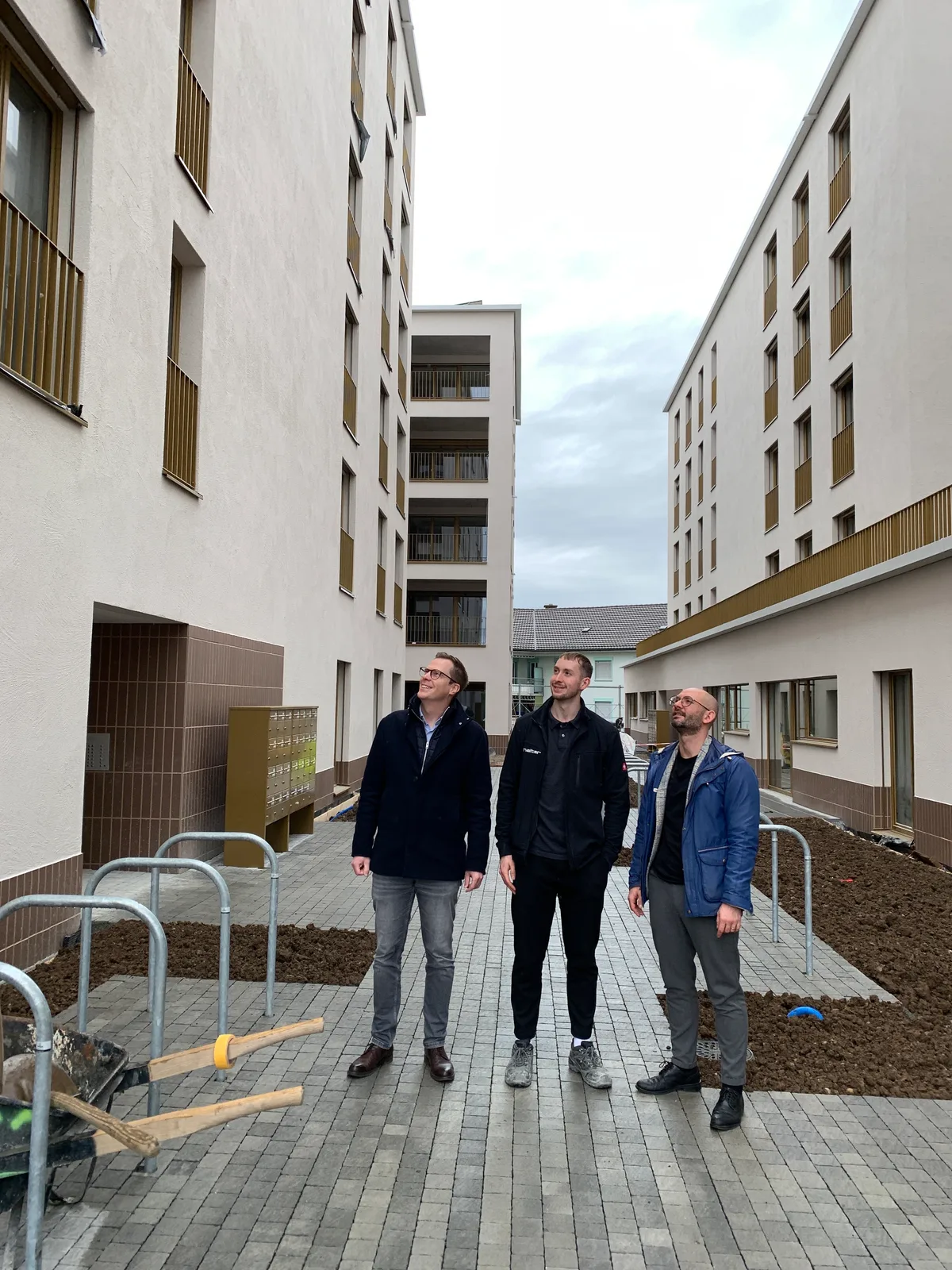 Drei Männer stehen in einer Häuserschlucht.