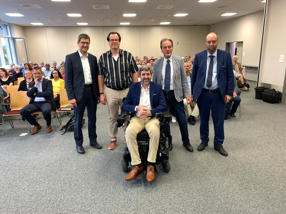 Fünf Männer zeigen sich in einem Raum voller Leute.