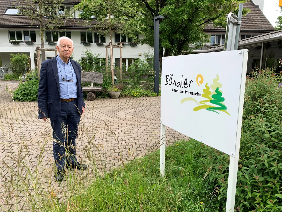 Ein Mann steht neben einer Hinweistafel vor einem Altersheim.