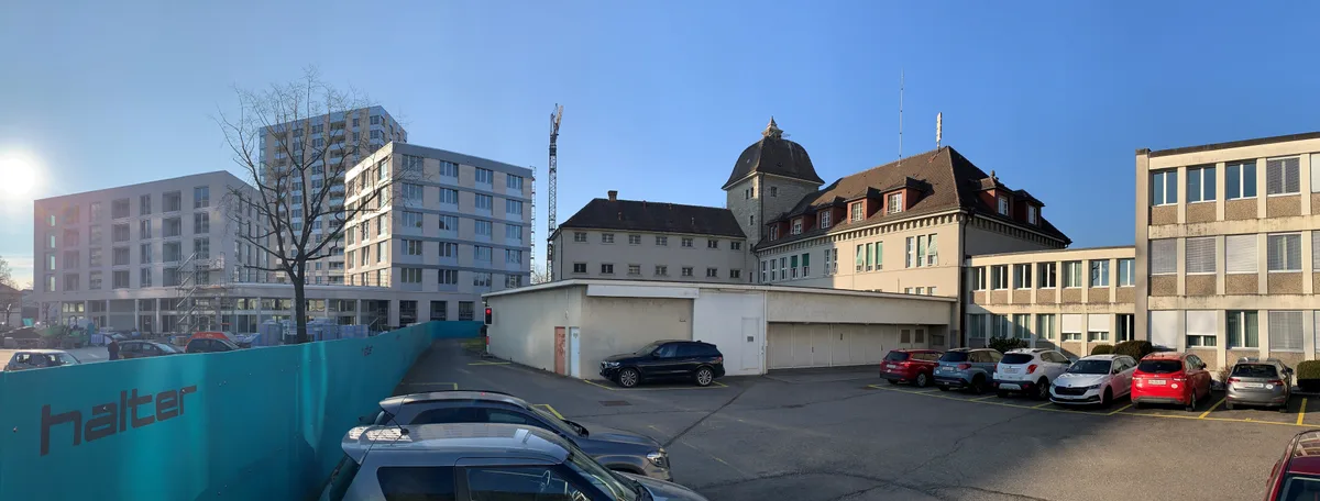 Neben dem Bezirksgericht Uster (Gebäude in der Mitte) sind nun Wohntürme hochgezogen worden. Anfang der 2030er Jahre wird der Kanton die Anbauten des Bezirksgebäudes (vorne und rechts) abreissen und Neubauten erstellen. Eine ganze Reihe von Wohnblöcken und Verwaltungsgebäuden und im Vordergrund ein Parkplatz.