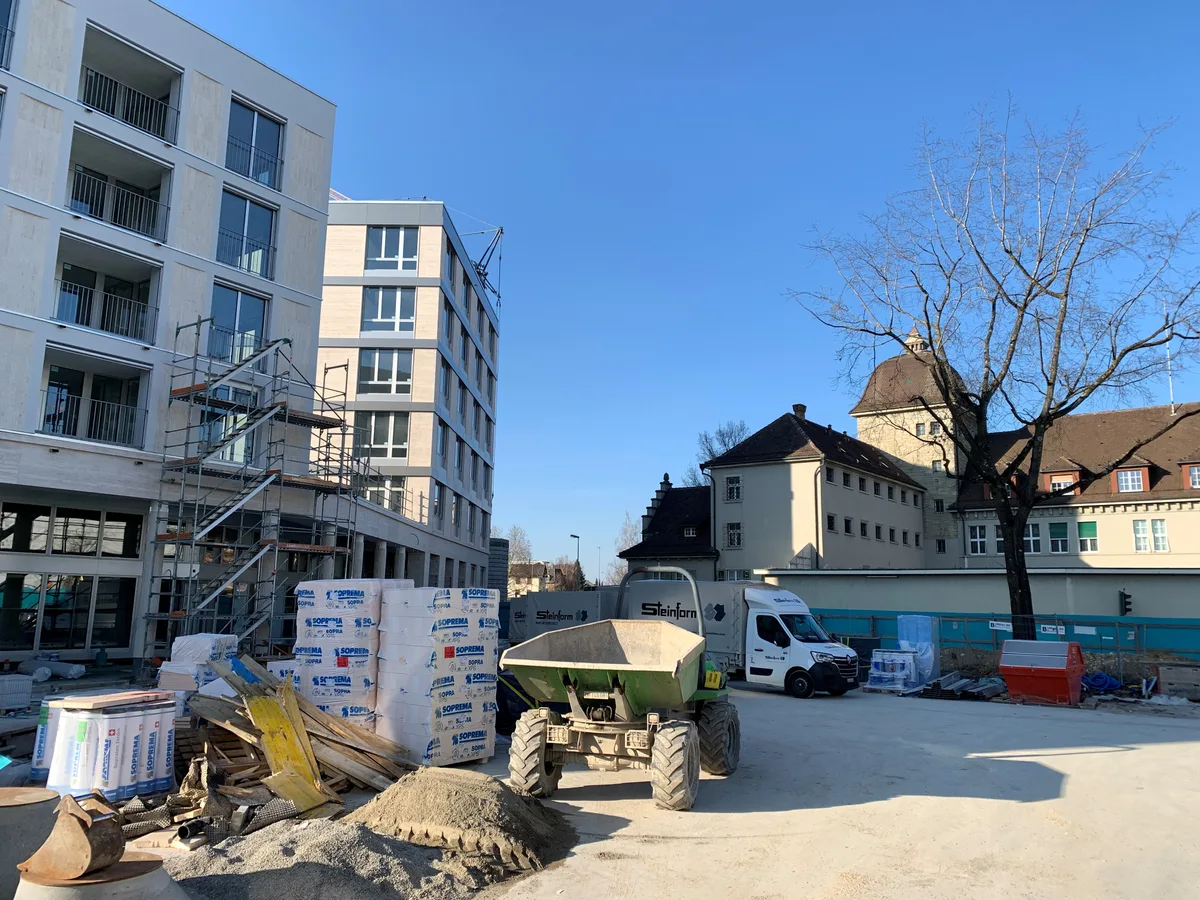Wo jetzt noch Material und Lieferwagen stehen, wird bis zum Sommer der neue Gerichtsplatz realisiert. Man sieht Baumaterial, einen Kipper sowie neue und alte Gebäude im Hintergrund.