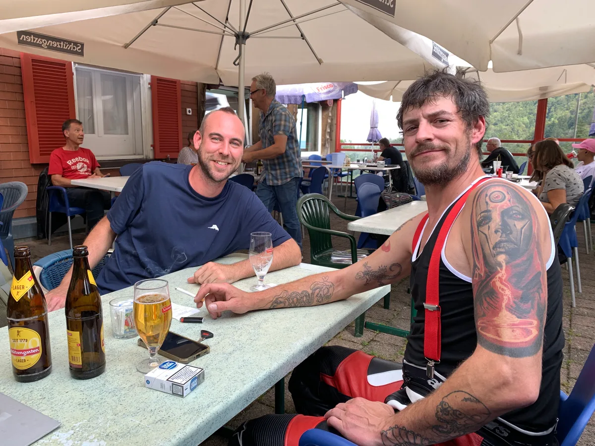 Zwei Männer sitzen im Restaurant an einem Tisch und schauen in die Kamera.