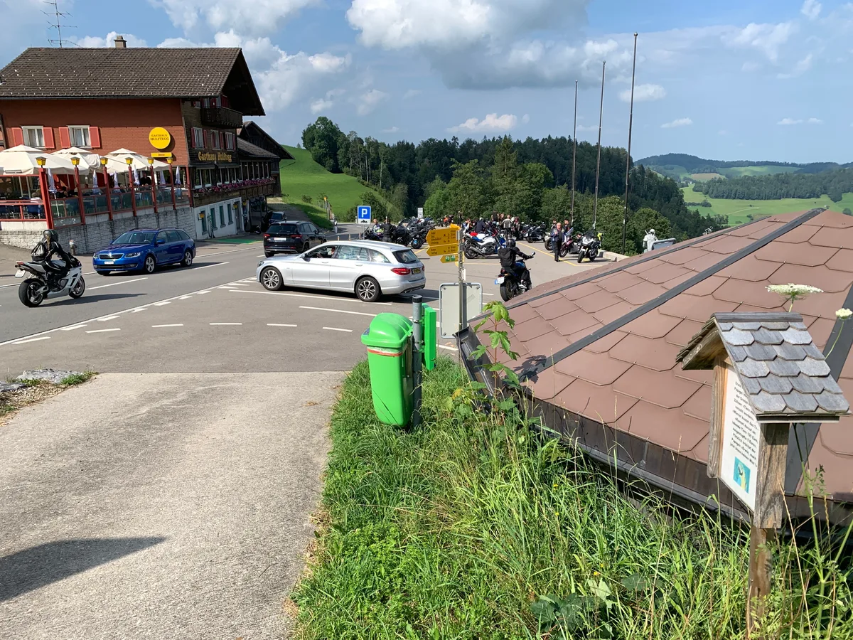 Das Gasthaus Hulftegg mit Autos, Töffs und einer Tafel des Witzwegs.