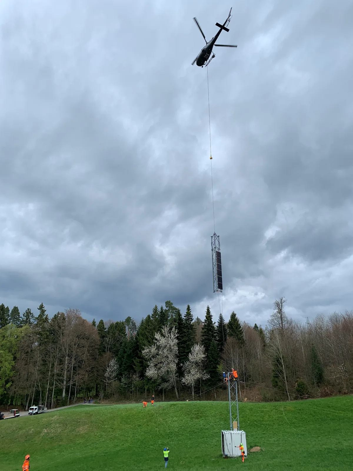 Ein Helikopter fliegt mit einem Teil eines Metallmasts davon.