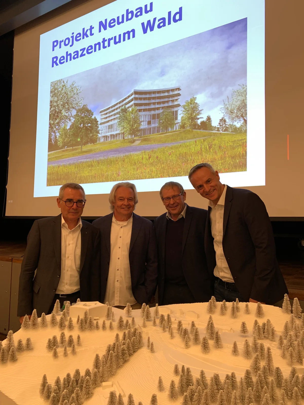 Vier Männer hinter dem Modell der neuen Reha-Klinik Wald.