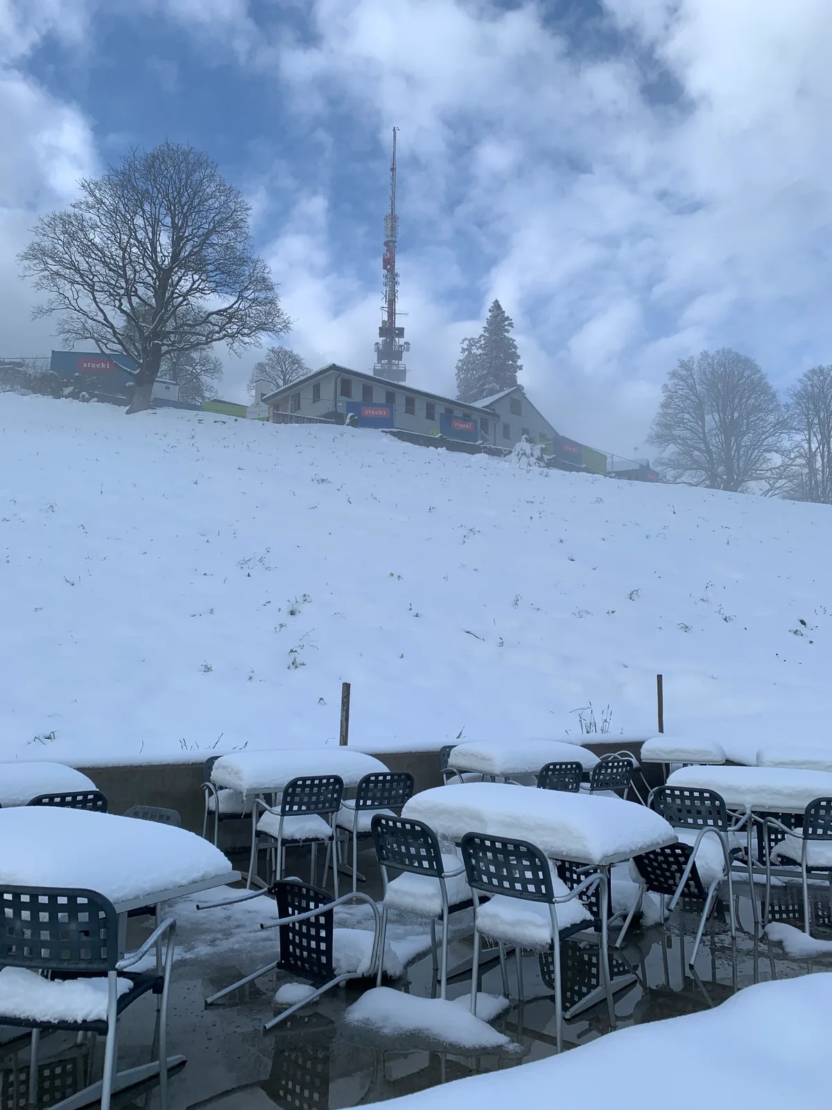 Restaurantsitzplatz ist von Schnee bedeckt, im Hintergrund Restaurant und Turm auf dem Bachtel.
