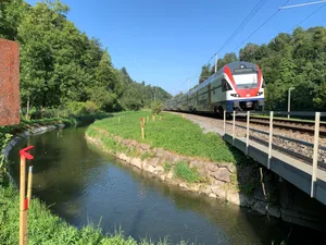 27169328-3 Markierungen für Doppelspurausbau der Bahnstrecke durchs Aatal zwischen den Bahnhöfen Uster und Aathal, Aufnahmen vom 18. August 2025; im Bild: Zug überquert eine kleine Brücke über den Aabach-Kanal beim Purpelgraben