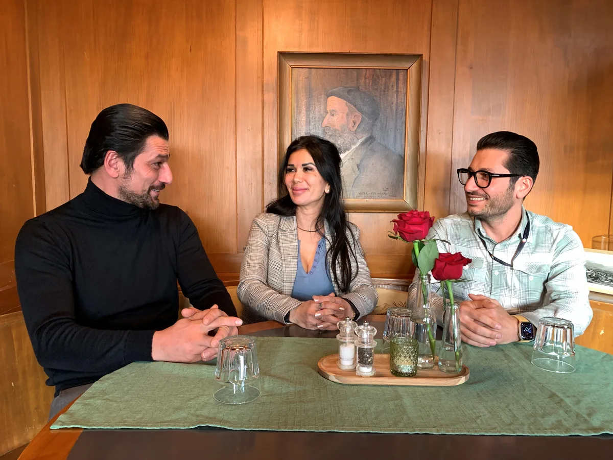 Eine Frau und zwei Männer sitzen an einem Wirtshaustisch.