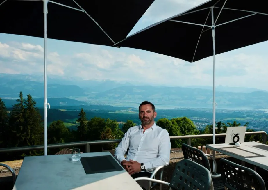 Man sitzt unter Sonnenschirmen auf einer Terrasse. 