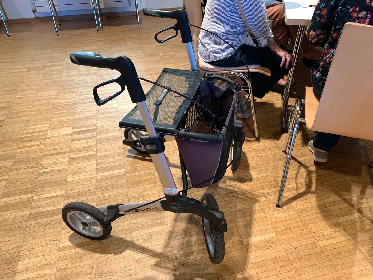 Ein Rollator steht neben einigen sitzenden Personen.
