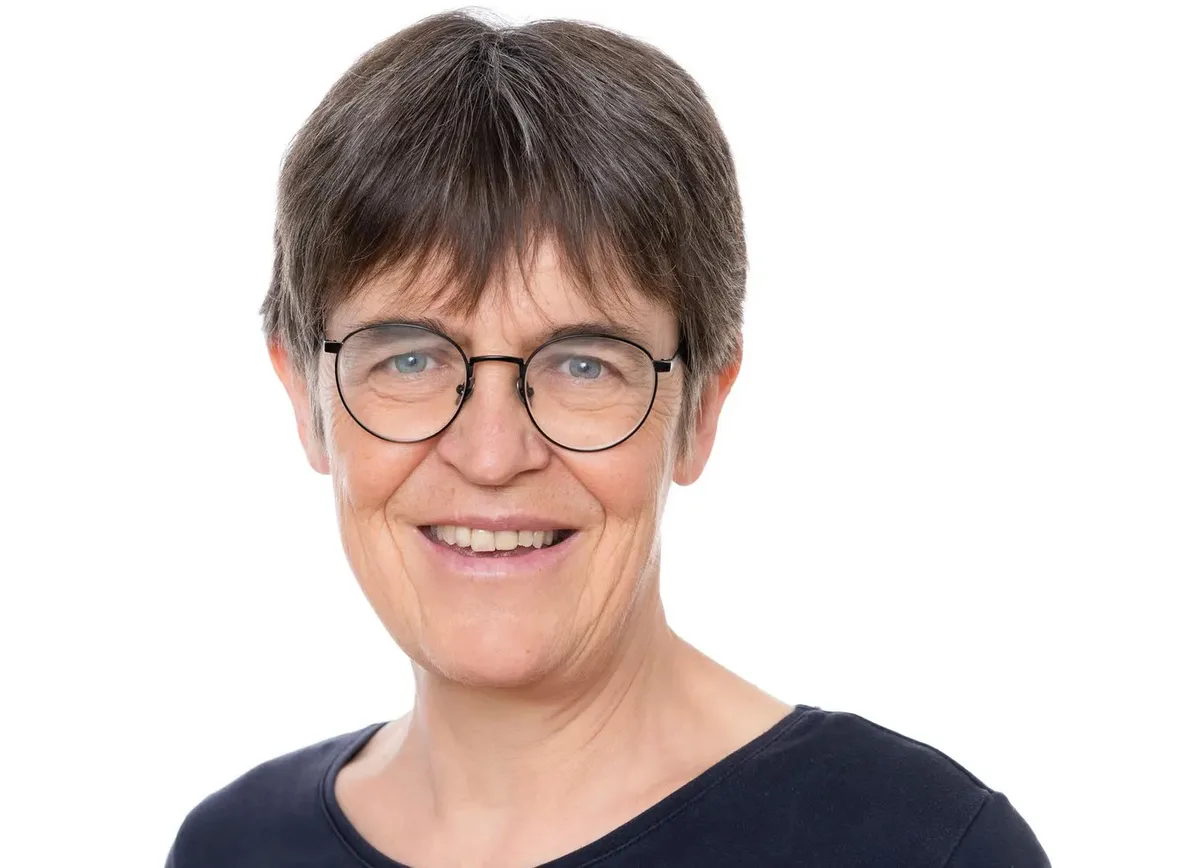Eine Frau mit kurzen Haaren und Brille lächelt in die Kamera.