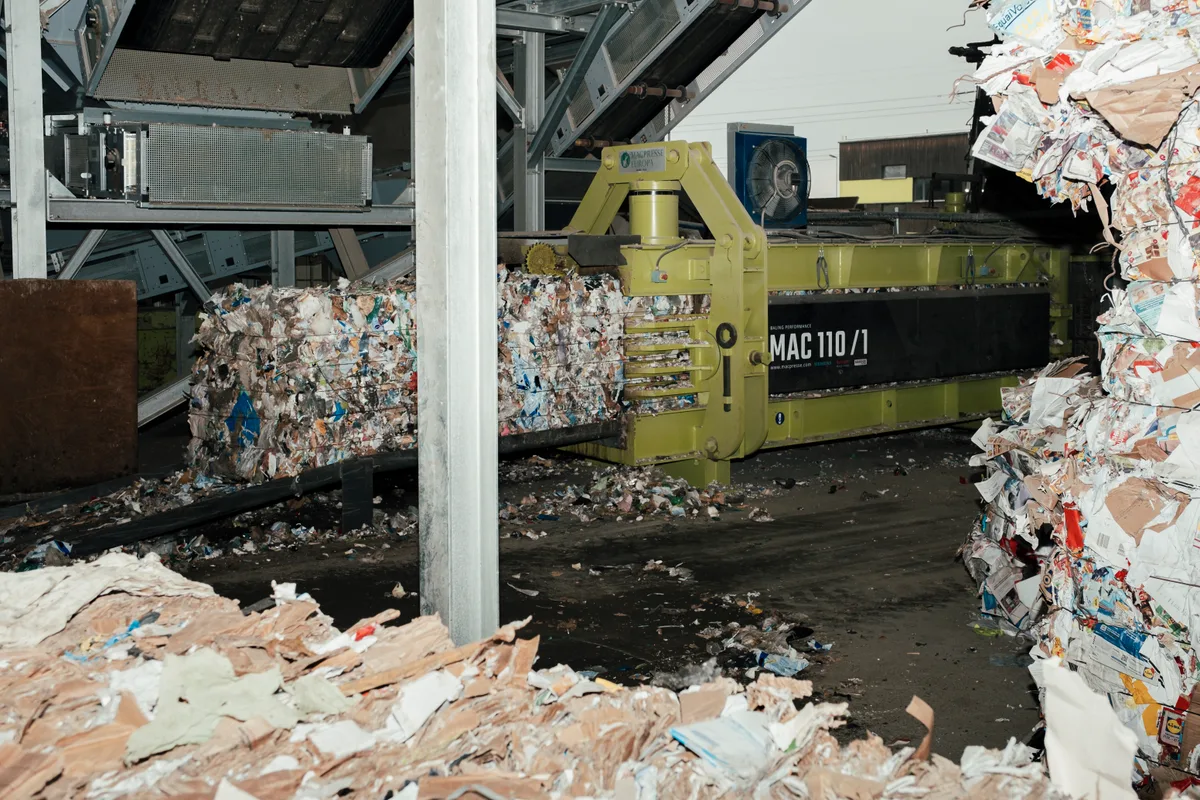 Eine grüne Presse spuckt ein Recyclingquader aus.