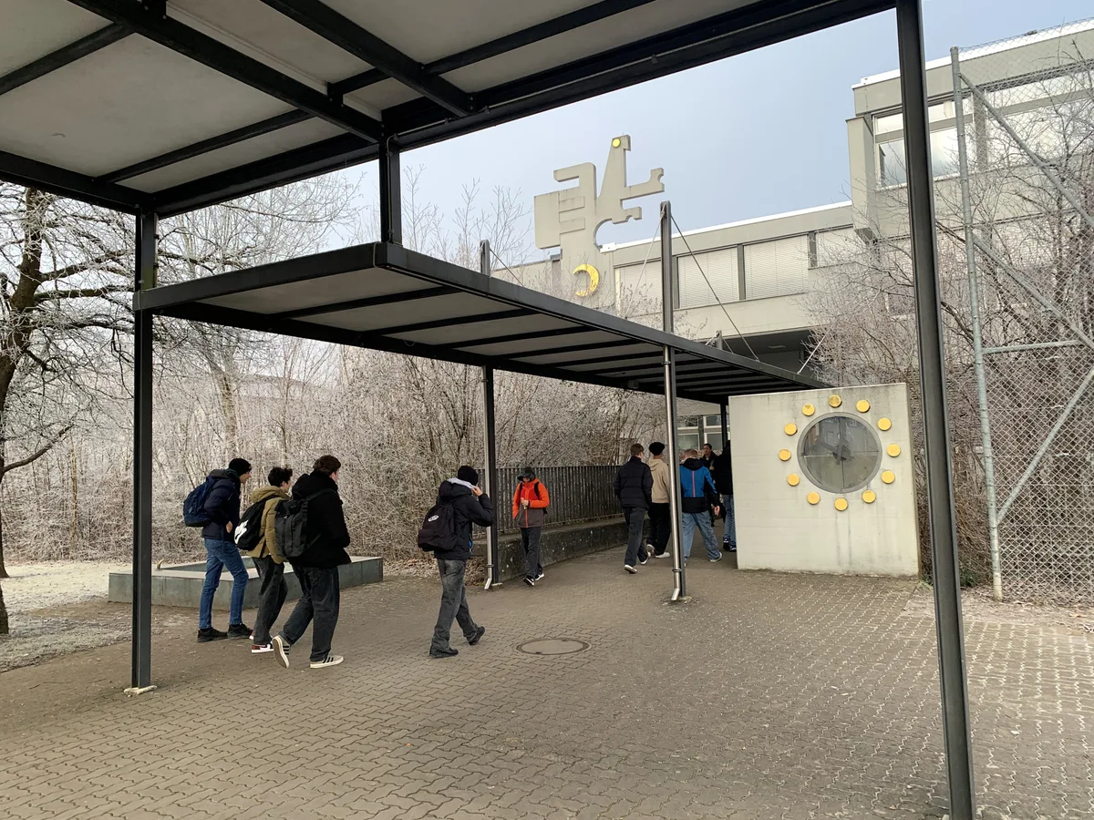 Mehrere Schüler gehen unter einem überdachten Weg in ein Schulhaus.