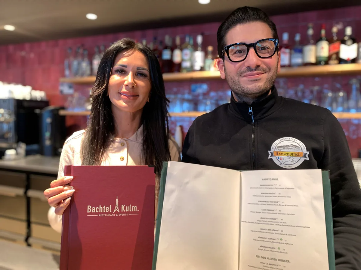 Kleine, aber feine Karte: Ayse Baskapan führt den Service im «Bachtel-Kulm», Sahin Albas (rechts) kümmert sich im Hintergrund um die Administration und das Marketing. Im neuen Restaurant Bachtel-Kulm halten Ayse Baskapan (links) und Sahin Albas die Wein- und die Speisekarte hoch.