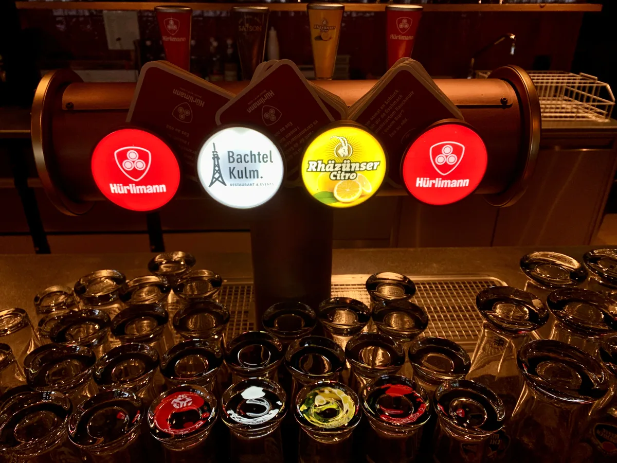Das Signet des neuen Restaurants Bachtel-Kulm reiht sich am Zapfhahn neben Bier- und Citro-Marken ein. Man sieht einen Zapfhahn und diverse Gläser.