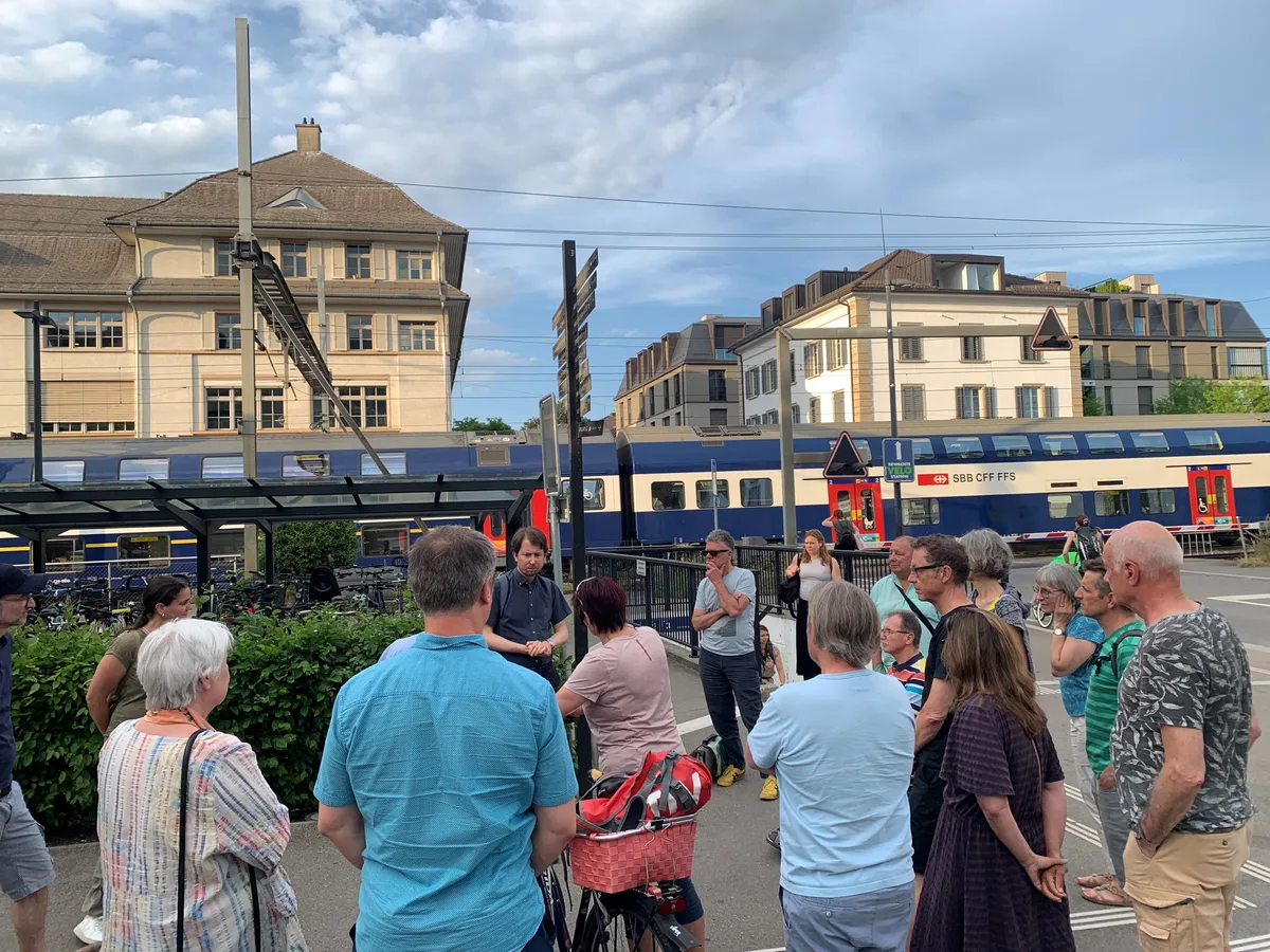Während ein Zug vorbeifährt, stehen Leute in der Nähe des Bahnübergangs beim Bahnhof Uster. 