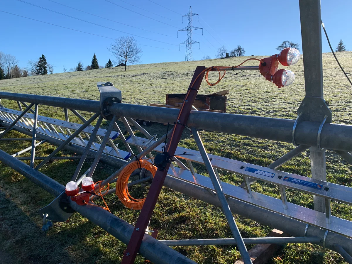 Auf einer Wiese liegt ein Teil eines Masts mit einer Leuchte.