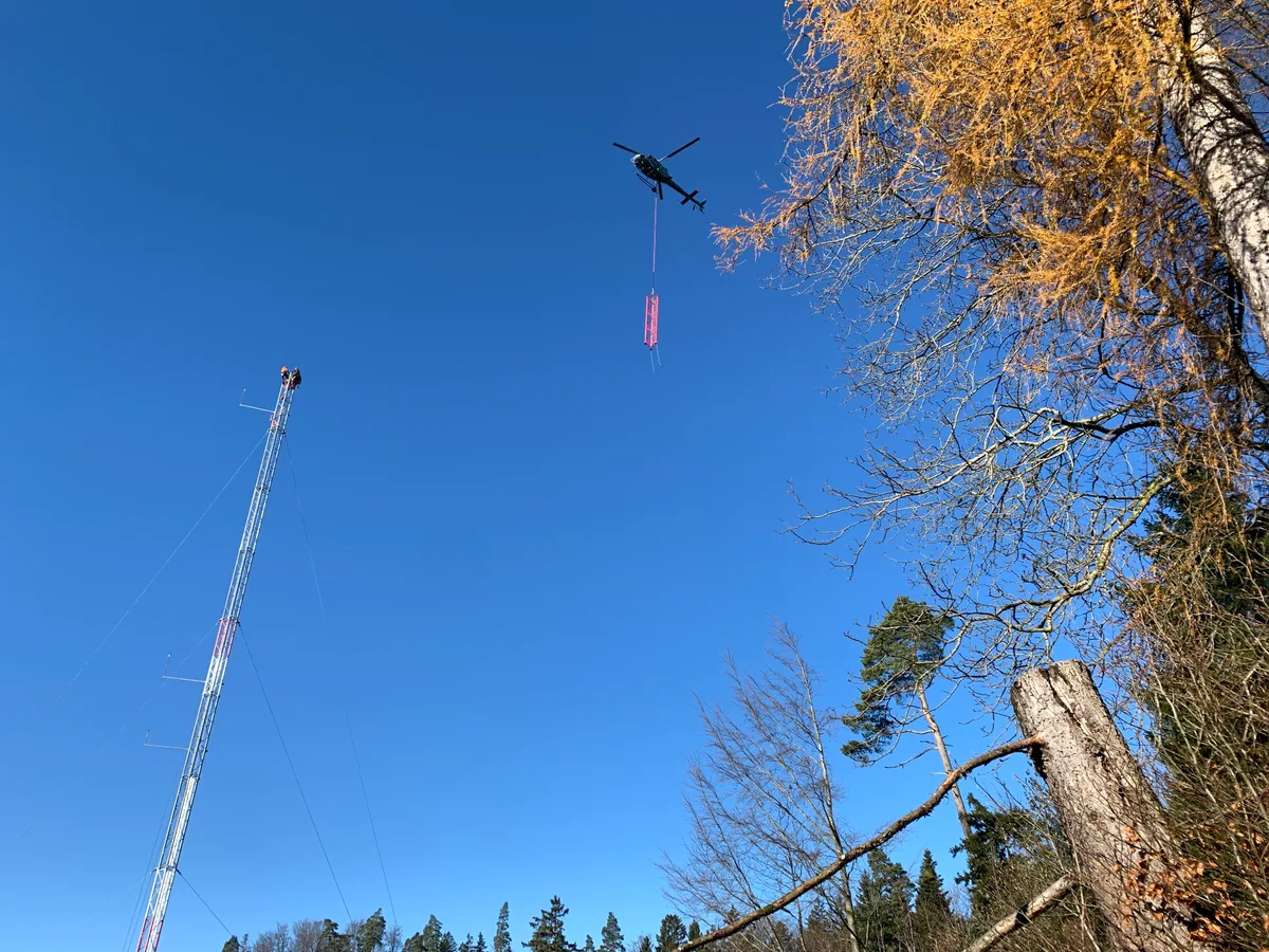 Ein Helikopter transportiert ein Teil eines Masts.