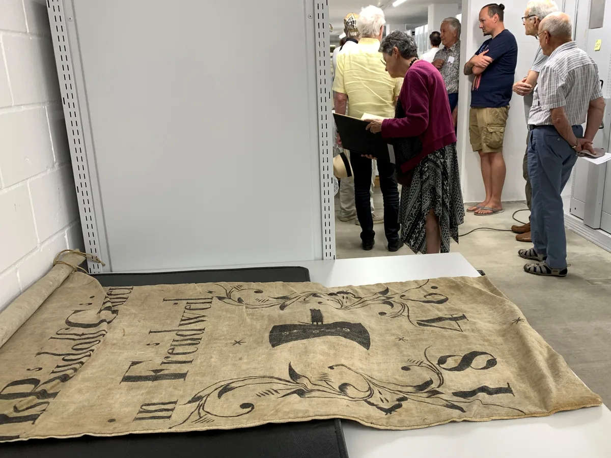 Ein Mehlsack aus dem Jahr 1846 liegt auf einem Tisch, während im Hintergrund Leute zu einem grossen Regal schauen.