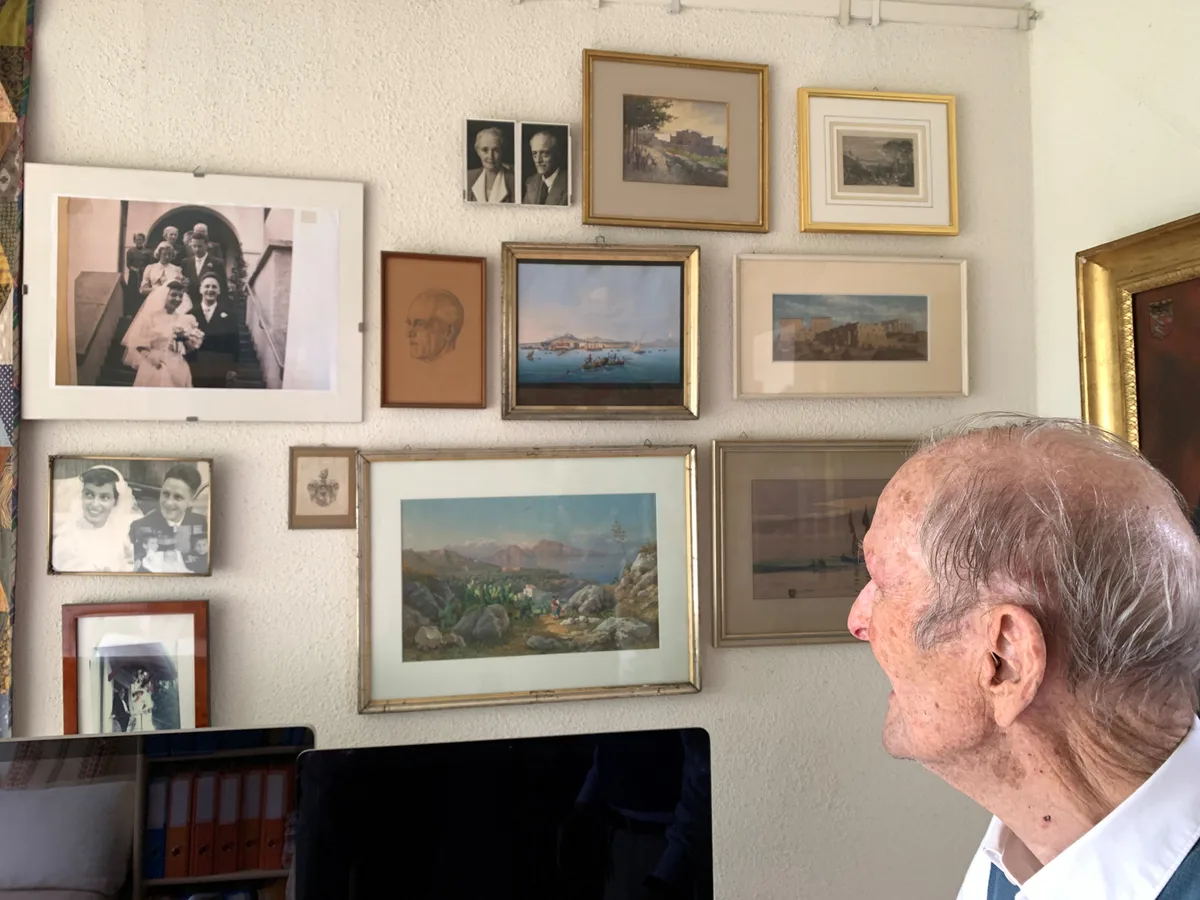 Ein Mann blickt auf verschiedene Bilder, die an der Wand hängen.