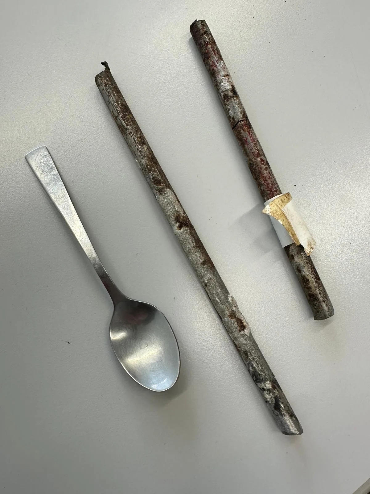 Man sieht einen Löffel neben zwei verrosteten Metallstabbruchstücken.