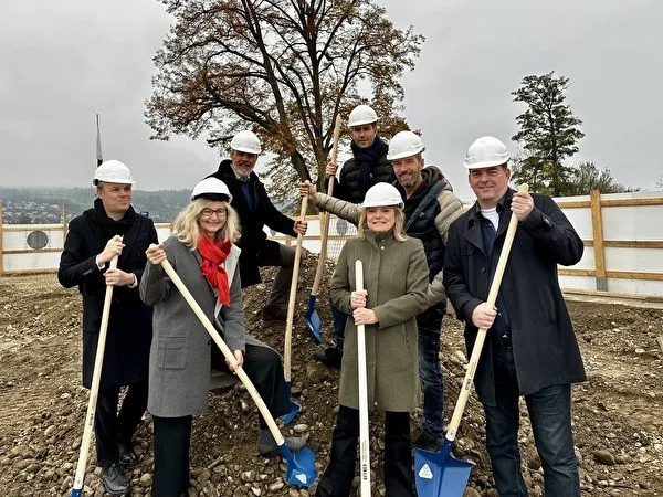 Eine Gruppe steht mit Schaufeln auf einer Baustelle.