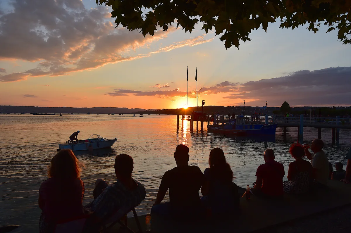 Menschen blicken am See in den Sonnenuntergang.