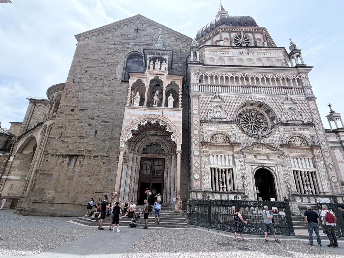 Die Cappella Colleoni in der Altstadt von Bergamo. Menschen stehen und sitzen auf einer Treppe vor der Barockkirche Cappella Colleoni.