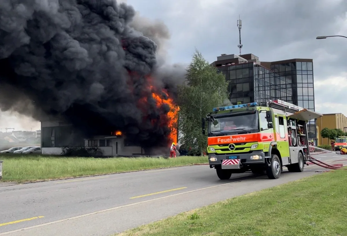 Feuerwehrfahrzeug vor lichterloh brennendem Gebäude mit schwarzer Rauchsäule