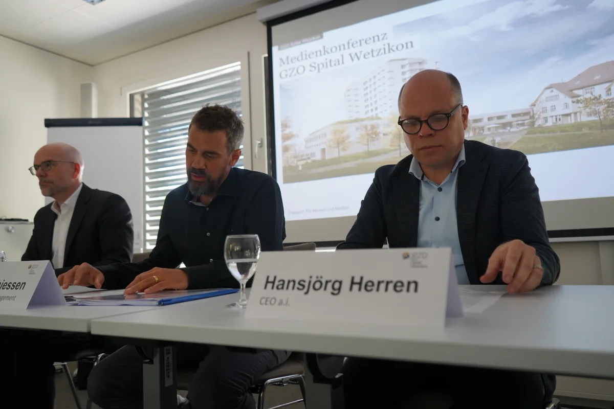 Drei Männer sitzen an einer Pressekonferenz hinter weissen Tischen.