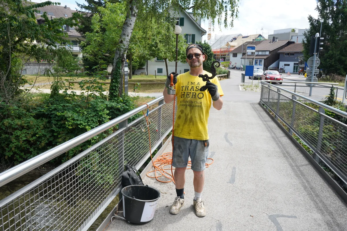 Mann steht auf einer Brücke und präsentiert ein Stück Metall.