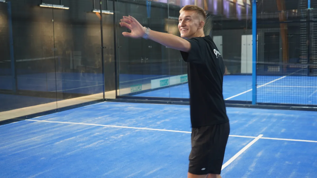 Ein Mann mit schwarzem T-Shirt spielt auf einem Padel-Platz.
