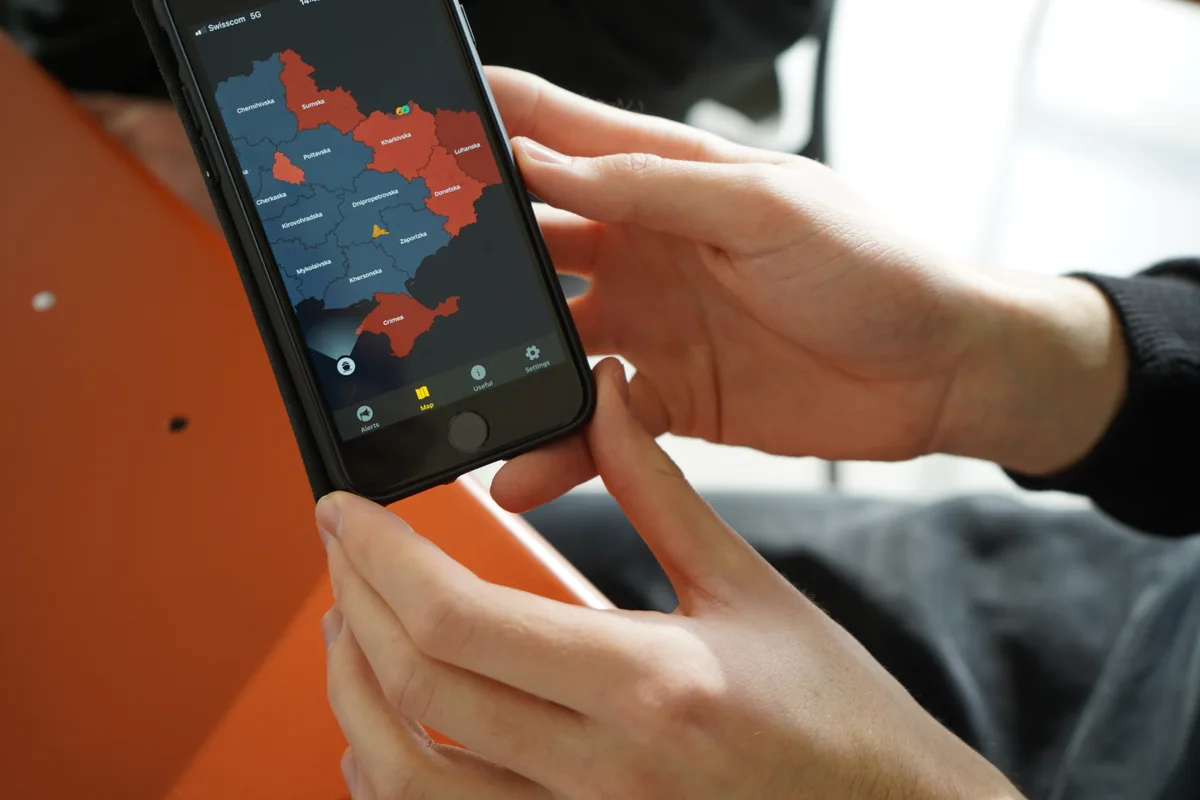 Hände, die ein Smartphone halten, mit der ukrainischen Karte drauf.