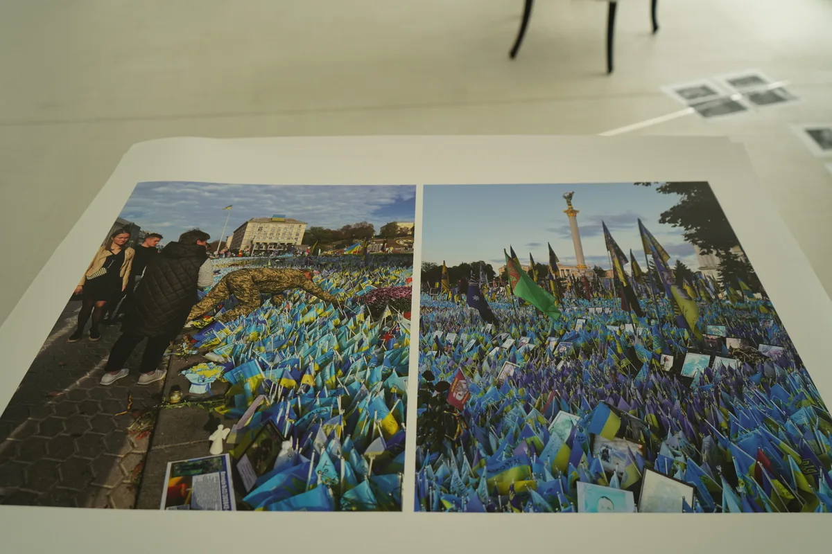Ein Plakat der Ausstellung mit einem Feld von ukrainischen Fähnchen auf einem Platz.