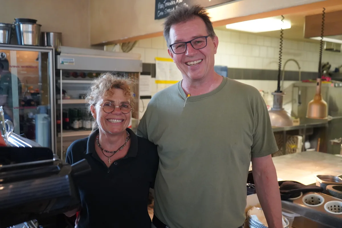 Eine Frau und ein Mann stehen in der Küche eines Restaurants und lächeln in die Kamera.