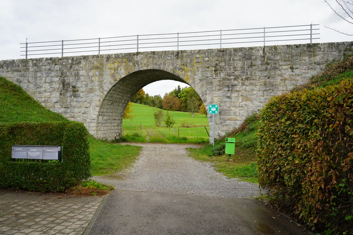 Ein Weg führt zu einem Bahndamm mit Rundbogen.