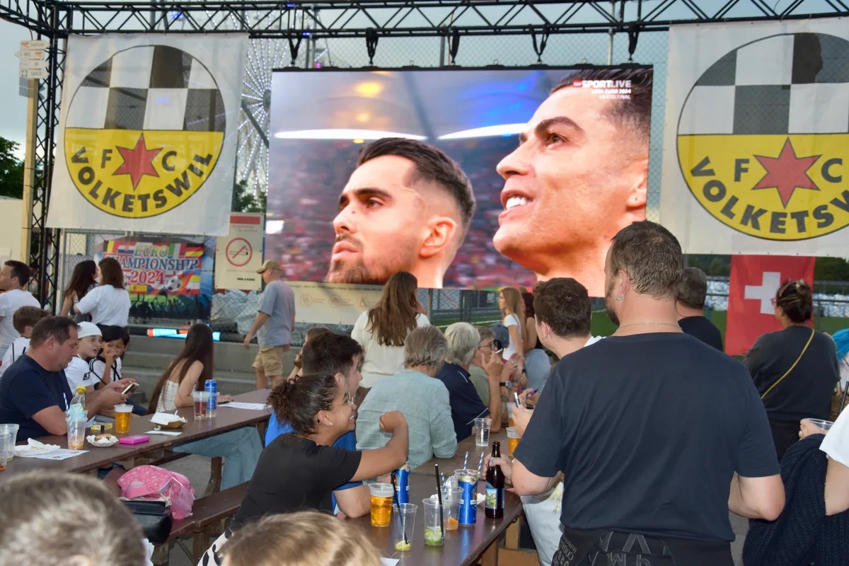 Ein Fussballspiel auf einem Bildschirm mit Menschen davor.