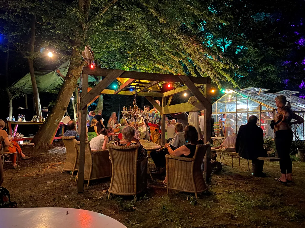Menschen, die abends unter einer bunten Lichterkette an einem Tisch sitzen.