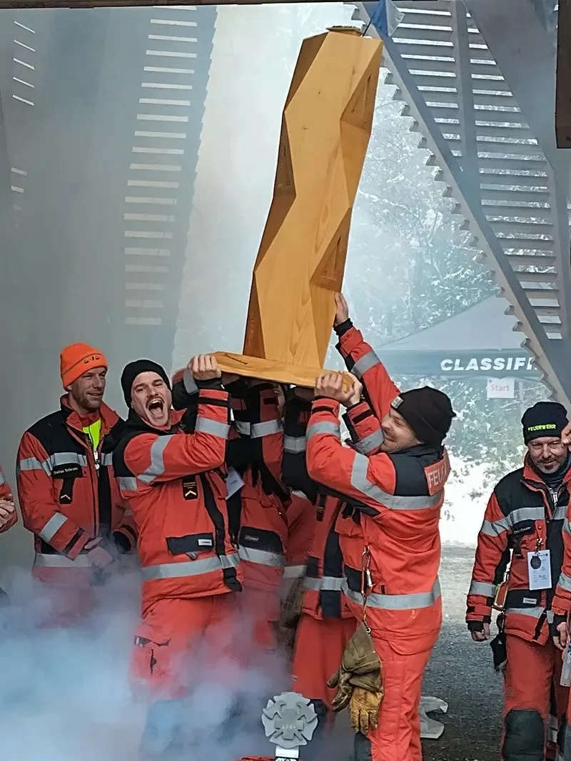Eine Gruppe von Feuerwehrmännern stemmt einen Holzpokal in die Luft.