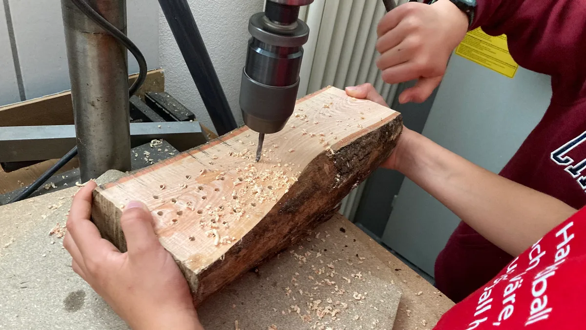 Kinderhände bohren mit einer Maschine Löcher in ein Holzscheit.
