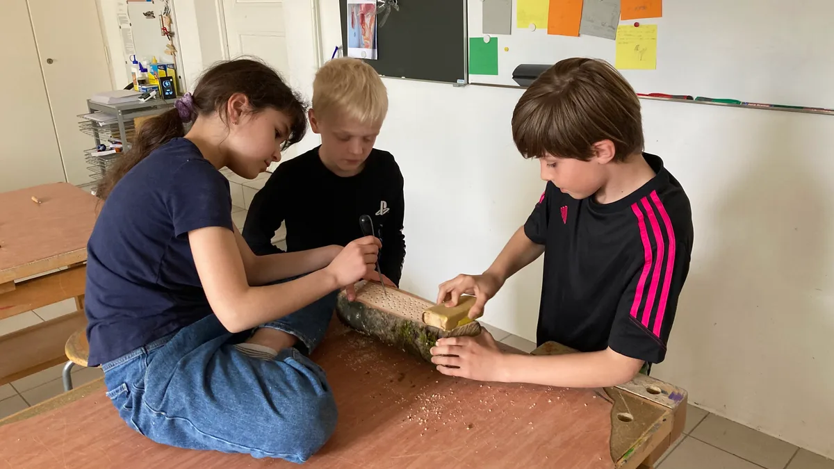 Kinder im Maurmer Primarschulhaus Pünt feilen an einem Holzscheit.