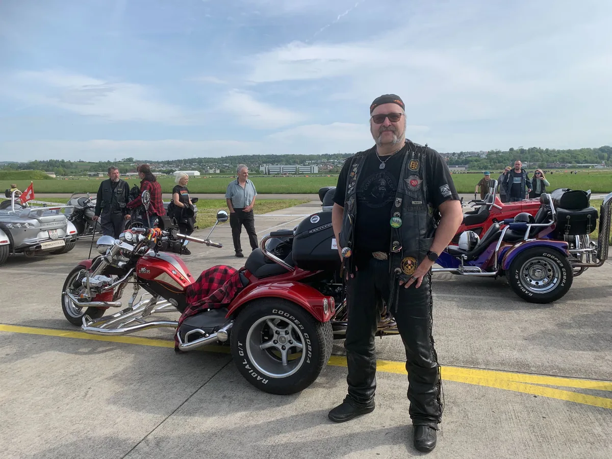 Ein Mann mit Schnauz vor einem dreirädrigen Motorrad.