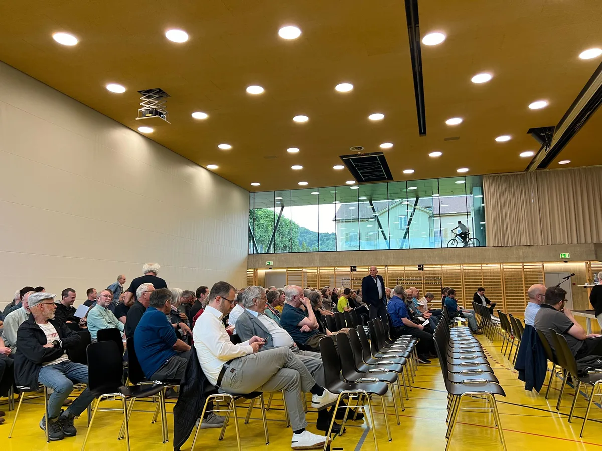 Menschen in einer Turnhalle auf Stühlen.